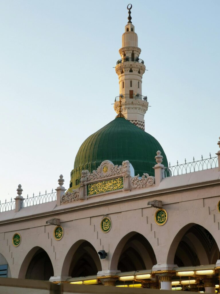 Detailed view of a mosque's green dome and minaret under the clear sky in Saudi Arabia.